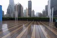 a wooden deck with metal bars and furniture in the rain over skyscrapers in the background