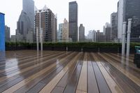 a wooden deck with metal bars and furniture in the rain over skyscrapers in the background