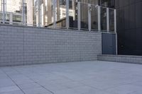 a large gray trash can next to tall buildings on a street near a fence with metal bars around it