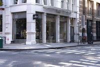 a woman wearing white and holding an umbrella crossing the street in front of a macy store