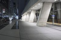an empty sidewalk in an urban city at night with several parked cars below it at a curb