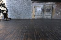 a room with wooden floors, a brick wall and an old machine wheel on the ground