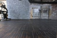 a room with wooden floors, a brick wall and an old machine wheel on the ground