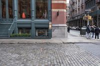 people walk by the sidewalk of a street corner, and look at a brick building in the background