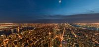 view of a city at night and the moon with the earth lite above the sky