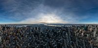 the view from a skyscraper overlooking new york city, at sunset time with sun peeking through clouds