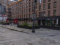 the city street has a couple of old buildings along it and tables and umbrellas in front of it