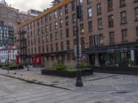 the city street has a couple of old buildings along it and tables and umbrellas in front of it