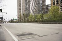 an empty city street with tall buildings in the distance and a few people crossing the street