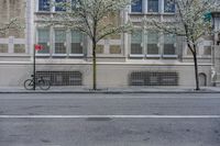 a bicycle parked along the side of a building by a tree filled street curb with no cars