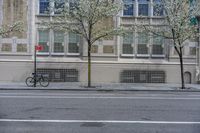 a bicycle parked along the side of a building by a tree filled street curb with no cars