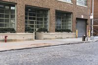 two fire hydrants on the sidewalk in front of a large brick building with many windows
