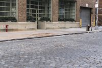 two fire hydrants on the sidewalk in front of a large brick building with many windows