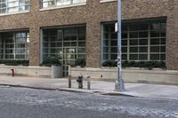 two fire hydrants on the sidewalk in front of a large brick building with many windows