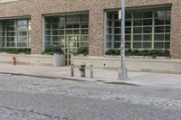 two fire hydrants on the sidewalk in front of a large brick building with many windows