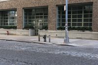 two fire hydrants on the sidewalk in front of a large brick building with many windows