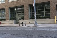 two fire hydrants on the sidewalk in front of a large brick building with many windows