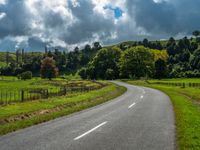 the asphalt road is winding towards a small town on a hillside overlooking a vast field