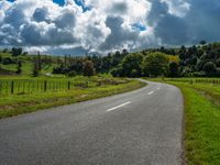 the asphalt road is winding towards a small town on a hillside overlooking a vast field