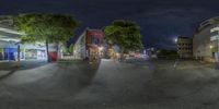 a city street filled with lots of trees in a town at night by itself with many buildings