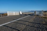 an empty highway on the coast and a sea behind it with a white fence in the middle of it