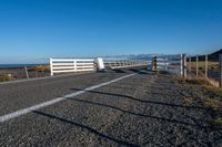 an empty highway on the coast and a sea behind it with a white fence in the middle of it