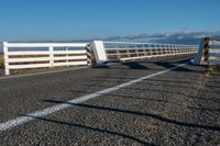 an empty highway on the coast and a sea behind it with a white fence in the middle of it