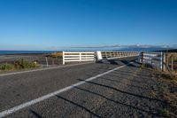 an empty highway on the coast and a sea behind it with a white fence in the middle of it