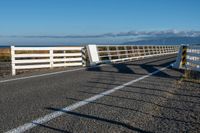 an empty highway on the coast and a sea behind it with a white fence in the middle of it