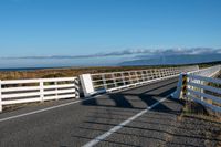 an empty highway on the coast and a sea behind it with a white fence in the middle of it