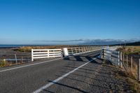 an empty highway on the coast and a sea behind it with a white fence in the middle of it