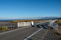 an empty highway on the coast and a sea behind it with a white fence in the middle of it