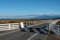 an empty highway on the coast and a sea behind it with a white fence in the middle of it