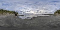 the view from below of a body of water on a beach with cliffs, grass and trees