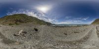 360 lens image of rocks and a large body of water under the sky and the sun