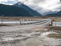 a train traveling over an open bridge that spans a river, near a mountain range