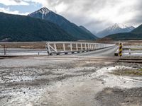 a train traveling over an open bridge that spans a river, near a mountain range