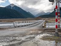 a train traveling over an open bridge that spans a river, near a mountain range