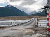 a train traveling over an open bridge that spans a river, near a mountain range