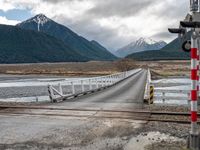 a train traveling over an open bridge that spans a river, near a mountain range