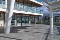 a large walkway leads to a building on the waterfront with windows open and view of sail boats