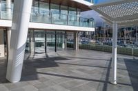 a large walkway leads to a building on the waterfront with windows open and view of sail boats