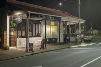 a street at night with a cafe in the corner and a bus coming out of it