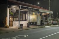 a street at night with a cafe in the corner and a bus coming out of it