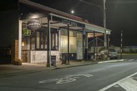 a street at night with a cafe in the corner and a bus coming out of it