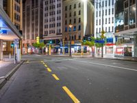 the night time image of an empty city street with buildings and pedestrians on it, which are not in the center of the photo