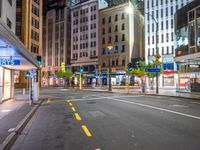 the night time image of an empty city street with buildings and pedestrians on it, which are not in the center of the photo