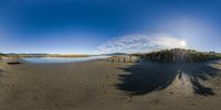 360 - spherical photograph of the beach with blue skies and clouds overhead, showing a sun reflecting in the water