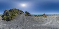 people walking along a dirt road through the middle of the ocean with large boulders in the background