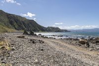 an empty beach with mountains on a sunny day near the ocean and water with stones